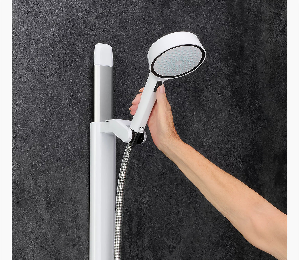Hand holding a white handheld shower head against a dark gray wall.