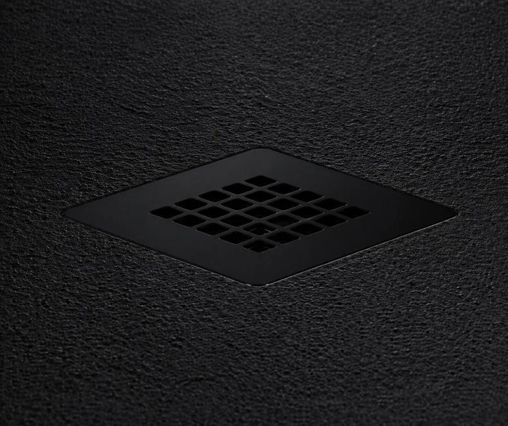 A matte black square drain cover with a grid of small square openings, set into a dark textured surface.