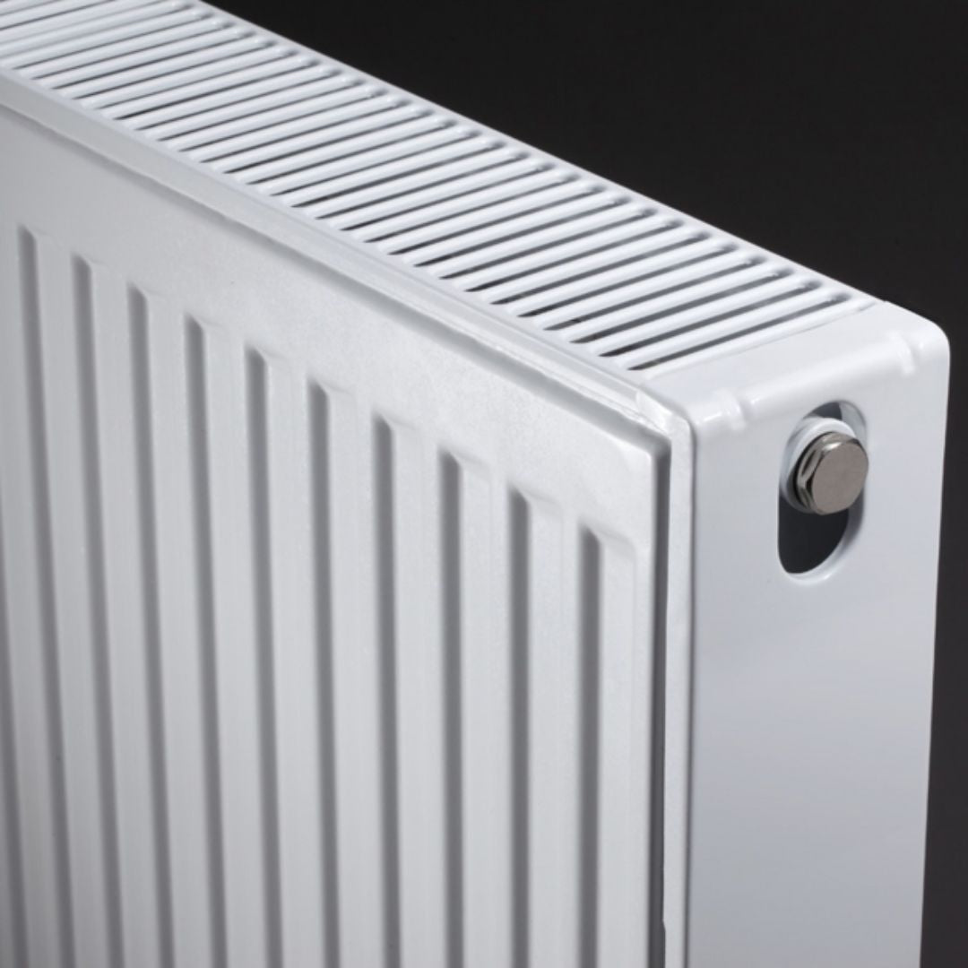 Close-up of a white metal radiator with vertical fins, a slotted top plate, and a silver valve nut on a dark background.