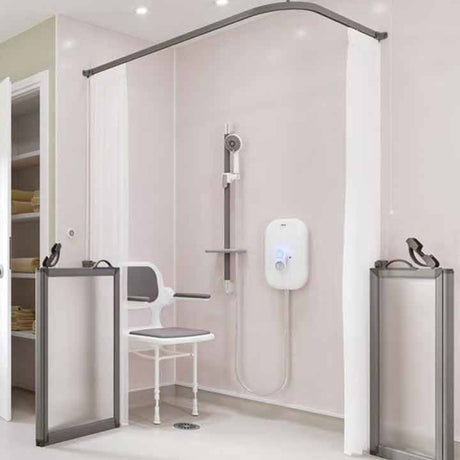 A modern shower bench setup in a bathroom, featuring a white shower chair with armrests, a wall-mounted shower head and hose, a white electronic water heater, white curtains, and gray-framed shower doors and handrails.