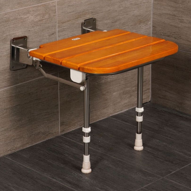 A wall-mounted shower bench with an oak wooden slatted seat and silver metal legs with white foot caps, shown installed against a gray tiled wall and floor.