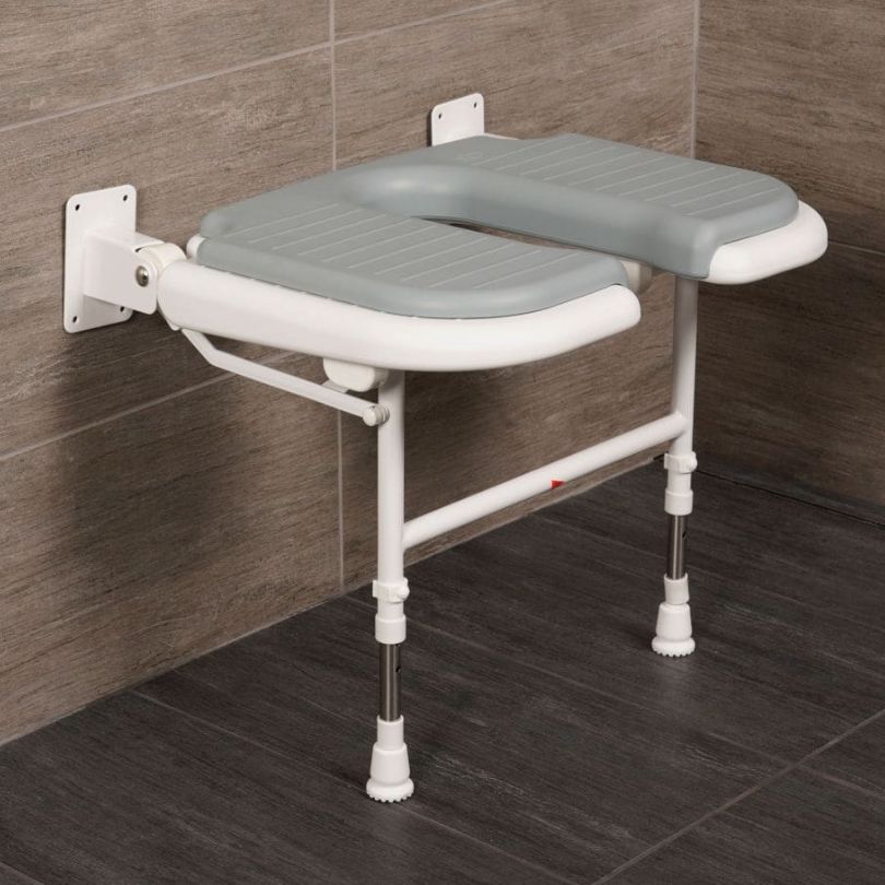 A wall-mounted bathroom safety seat with a gray molded seat cushion and white frame, shown attached to a tiled wall in a bathroom setting.