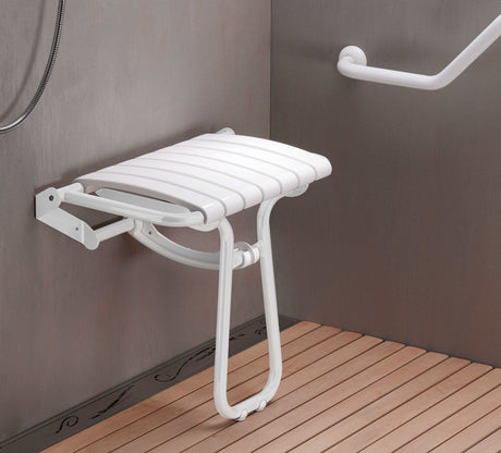 White folding shower seat mounted on a gray wall with a wooden floor.