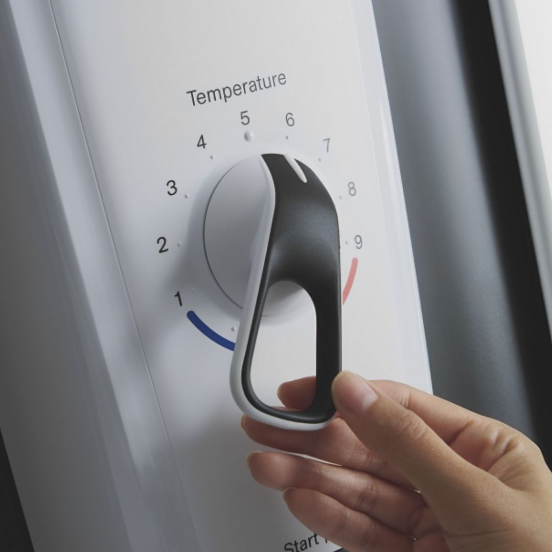 A close-up of a hand turning a black and white temperature control dial on a white shower appliance panel.