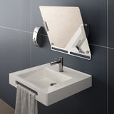A modern wall-mounted white sink with a chrome faucet, a gray towel hanging from the edge, and an attached rectangular mirror on a dark tiled wall.