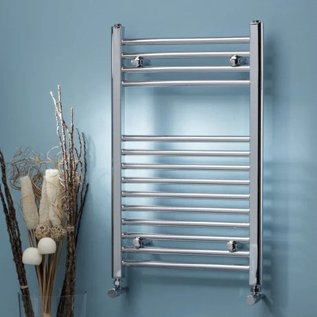 Chrome towel radiator mounted on a blue wall with decorative elements.