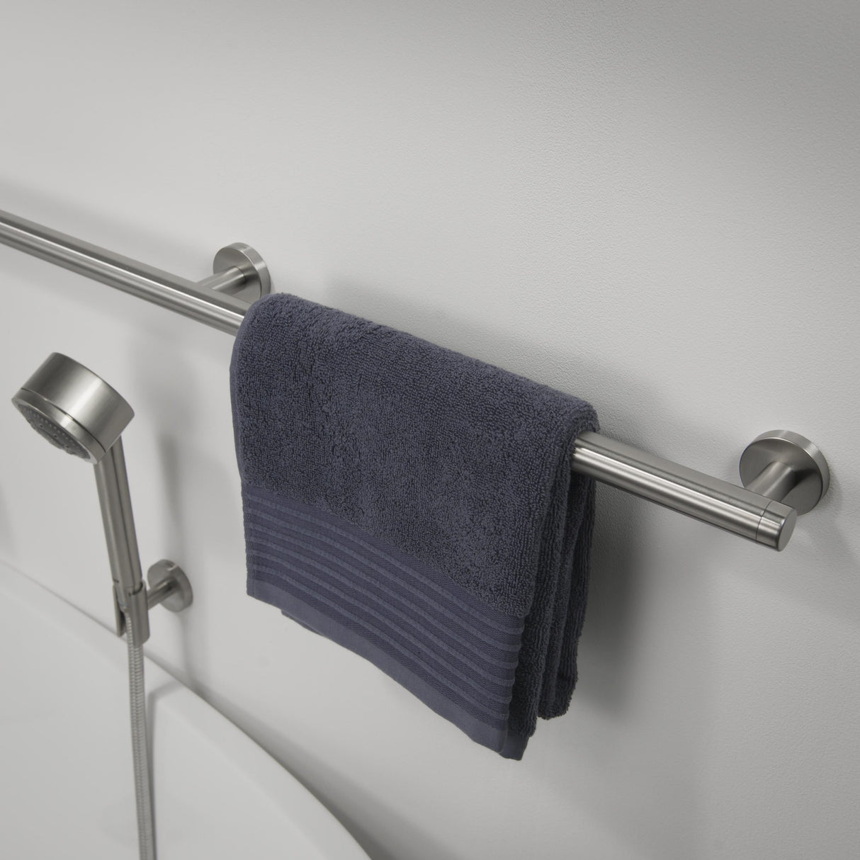 Gray towel hanging on a metal towel rack with a shower head in the background.