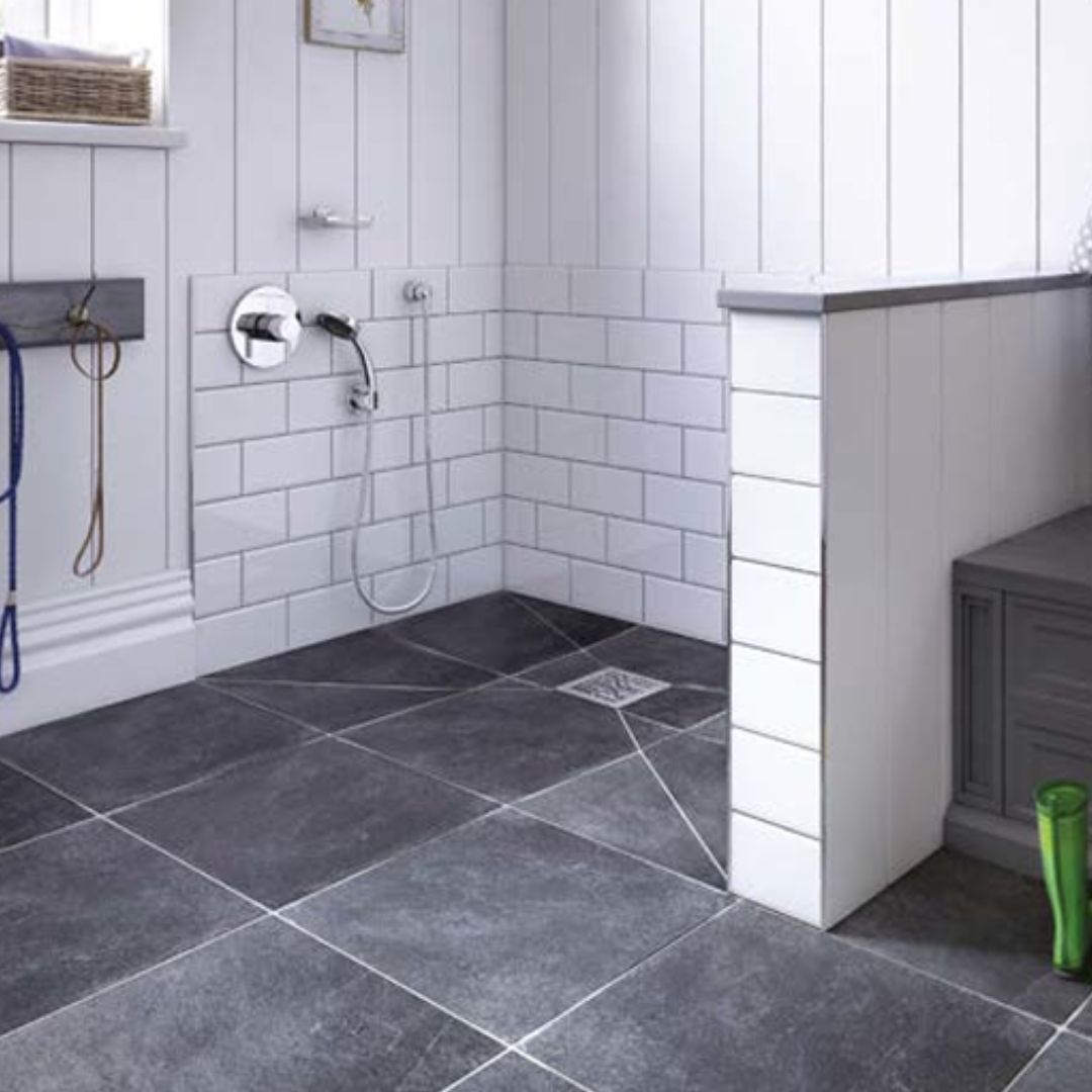 A modern bathroom corner with white shiplap walls, white subway tile wainscoting, dark charcoal gray stone floor tiles, a corner shower with chrome fixtures, and a gray vanity cabinet on the right.