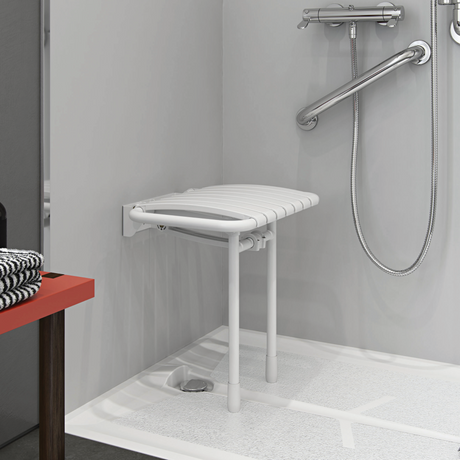 Foldable shower seat in a bathroom setting with a red stool and gray walls.