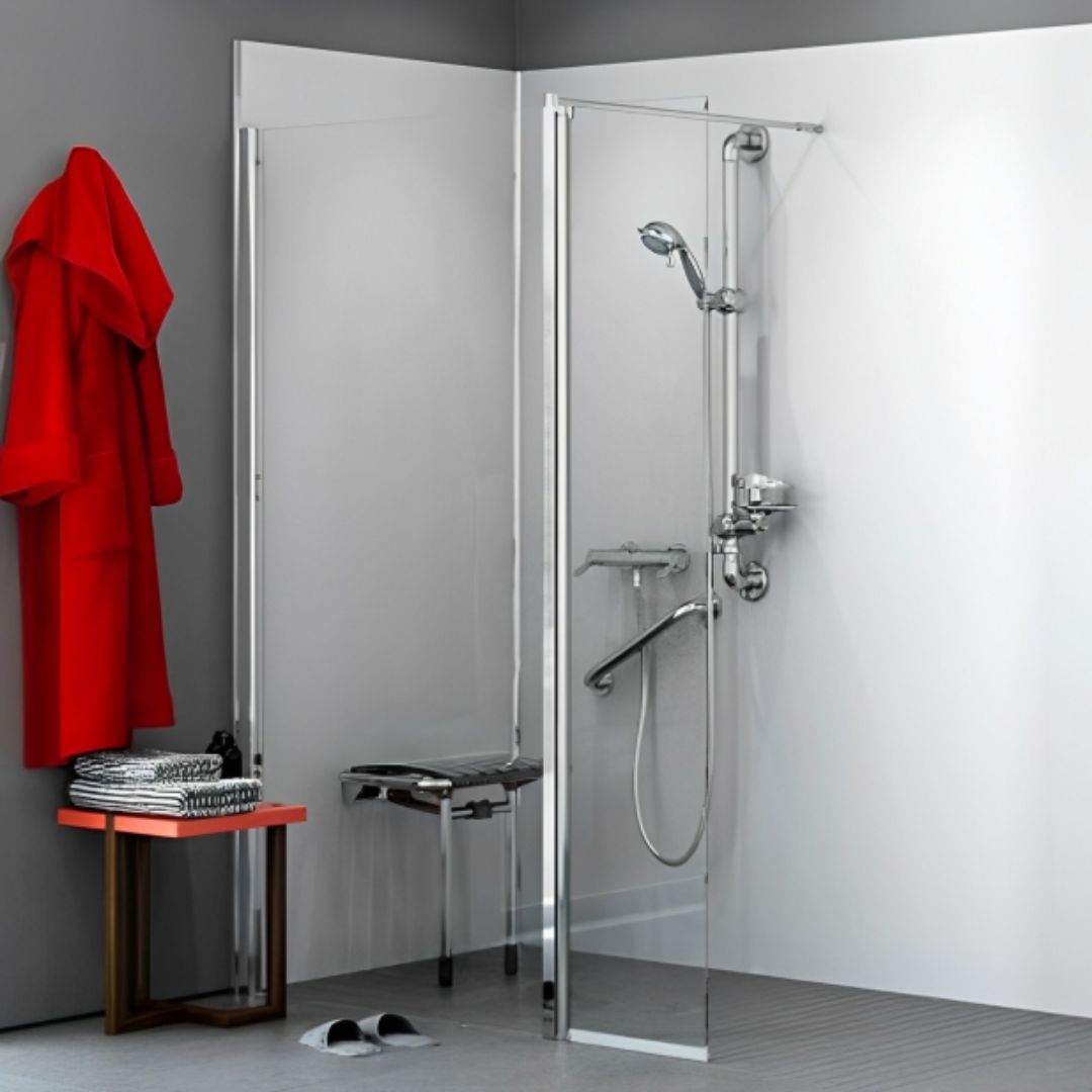 A modern corner shower enclosure with a clear glass door and chrome shower system, shown installed in a bathroom with gray walls, a red robe, a small table, and a bench.