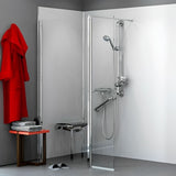A modern corner shower enclosure with a clear glass door and chrome shower system, shown installed in a bathroom with gray walls, a red robe, a small table, and a bench.
