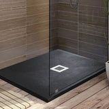 A modern shower base with a dark textured floor and a white square drain, enclosed by a clear glass door, set in a bathroom with brown wood-look tiles and flooring.