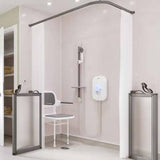 A modern shower bench setup in a bathroom, featuring a white shower chair with armrests, a wall-mounted shower head and hose, a white electronic water heater, white curtains, and gray-framed shower doors and handrails.