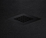 A matte black square drain cover with a grid of small square openings, set into a dark textured surface.