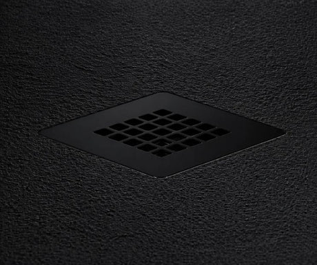 A matte black square drain cover with a grid of small square openings, set into a dark textured surface.