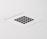 A square white metal floor drain cover with a grid pattern, set into a textured white plaster wall.