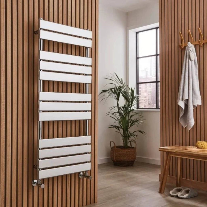 Chrome modern heated towel rail mounted on a wooden wall with a plant and bench in the background.