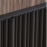 Close-up of a modern black pleated panel or grille with a dark top frame, shown against a wood-grain background.