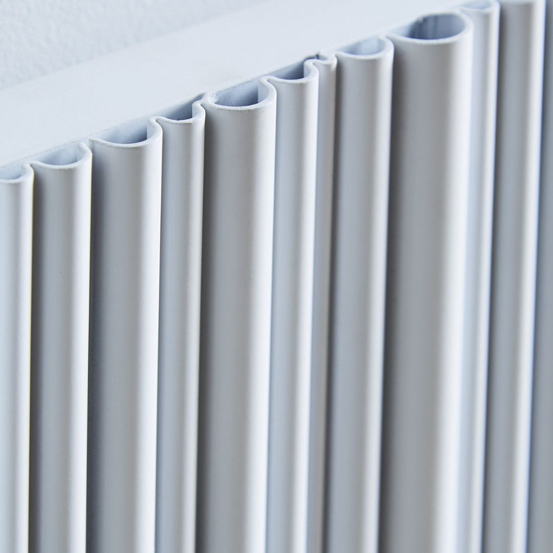 Close-up of a modern white pleated radiator panel hanging against a white wall.