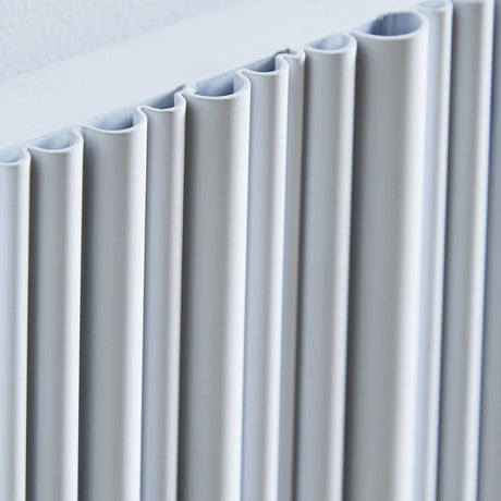 Close-up of a modern white pleated radiator panel hanging against a white wall.