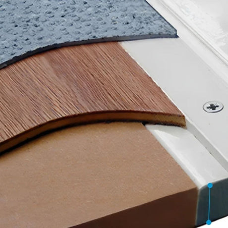 Close-up of a flooring or paneling material sample showing layered sections: a textured dark gray top layer, a medium brown woodgrain layer, a tan layer, and a white mounting or trim piece with a visible screw.