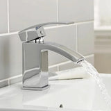 Chrome faucet with water flowing into a sink against a tiled bathroom wall.