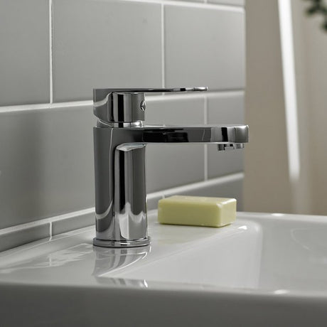Chrome faucet on a white sink with a bar of soap in a tiled bathroom.