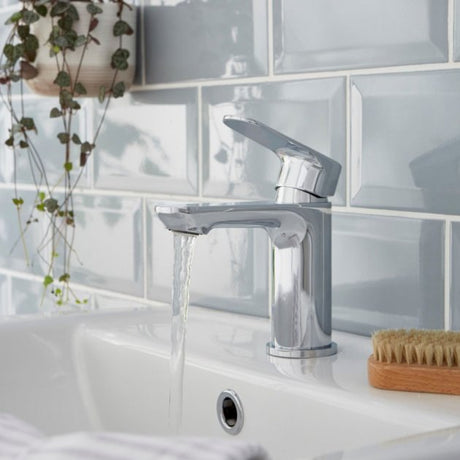 Chrome faucet on a sink with water flowing, against a tiled bathroom wall.
