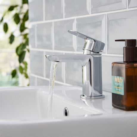 Chrome faucet on a sink with a bottle of soap next to it, against a tiled bathroom wall.