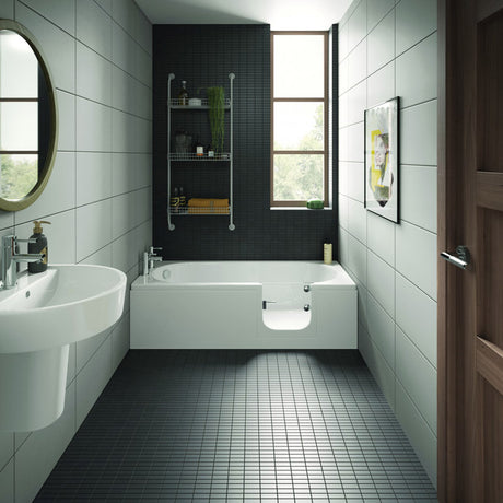 A modern bathroom interior with a white bathtub set into a dark tiled wall, white wall-mounted sink, black floor tiles, a round mirror, shelving, and a window.