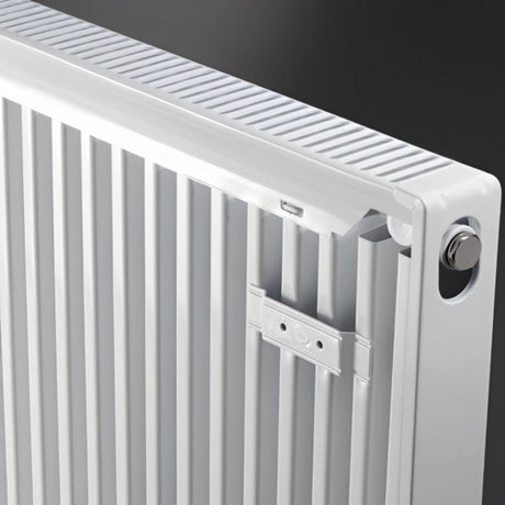 Close-up of a white metal radiator with vertical fins, a top cooling grille, and a silver adjustment knob against a dark background.