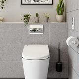 A modern white toilet with a flush button on the tiled wall, shown in a clean, contemporary bathroom setting with gray wall tiles, small potted plants, and a toilet brush holder.