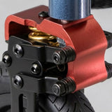 Close-up of a red anodized metal front fork mount with black hardware, a gold coil spring, and a blue metallic stem on a black wheel.