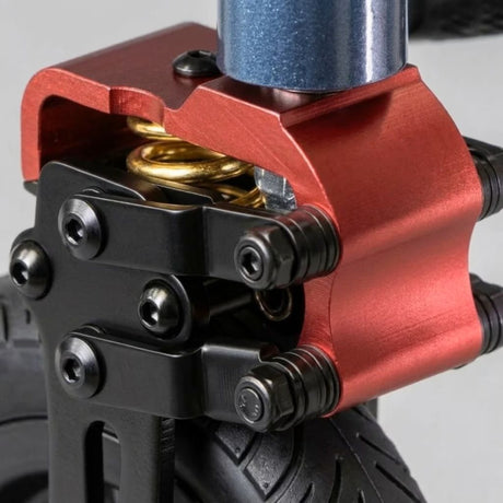 Close-up of a red anodized metal front fork mount with black hardware, a gold coil spring, and a blue metallic stem on a black wheel.
