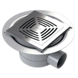 A square tiled stainless steel wetroom waste with a slotted grate cover, set inside a round gray drain flange with a gray pipe outlet.
