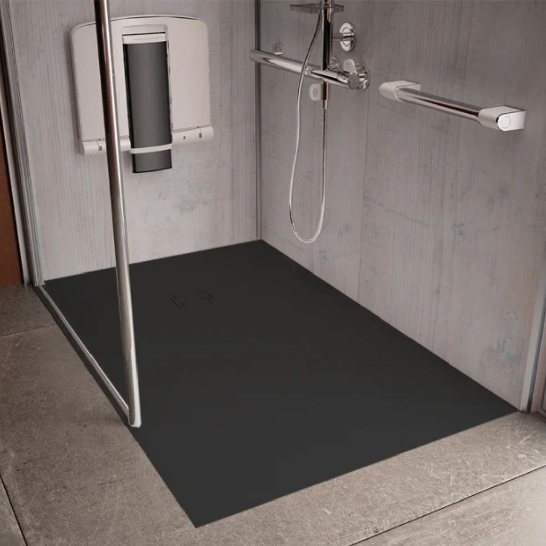 A black rectangular shower floor mat installed in a modern gray tiled shower stall with a glass door, chrome grab handles, and a wall-mounted shower seat.