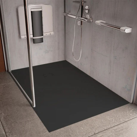 A black rectangular shower floor mat installed in a modern gray tiled shower stall with a glass door, chrome grab handles, and a wall-mounted shower seat.