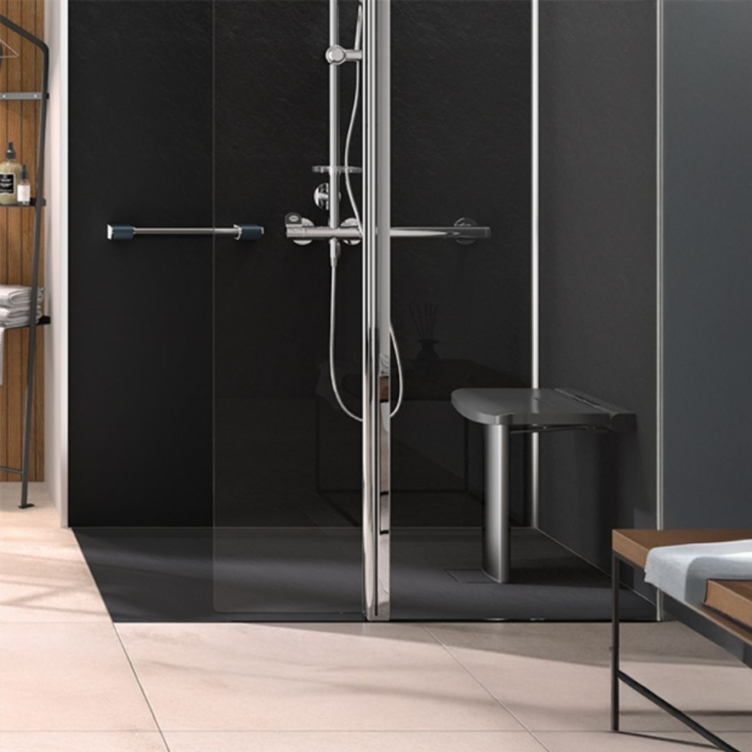A modern walk-in shower enclosure with a glass door and a chrome metal frame and hardware, shown installed in a contemporary bathroom with light beige tile floors and dark gray walls.