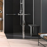 A modern walk-in shower enclosure with a glass door and a chrome metal frame and hardware, shown installed in a contemporary bathroom with light beige tile floors and dark gray walls.