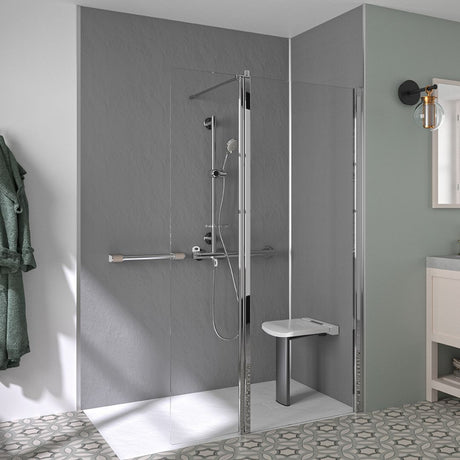 A modern walk-in shower enclosure with a clear glass door and frame, chrome shower hardware, a white bench seat, and gray textured walls in a bathroom setting.