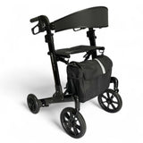 A black four-wheel rolling walker with a padded backrest, seat, and a matching black storage bag featuring a reflective silver stripe, shown on a white background.