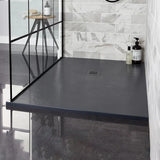 A dark charcoal gray slate-look shower traywith a built-in drain, installed in a modern walk-in shower with gray marble-look tiles and a black-framed glass door.