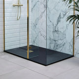 A modern glass shower enclosure with gold-toned metal frames and a matte black floor, shown installed in a bathroom with white subway tile and a white marble-patterned wall.