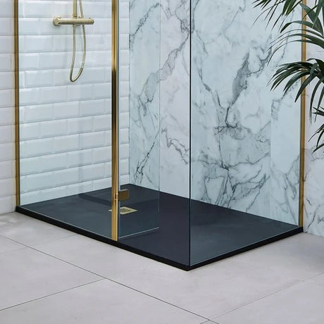 A modern glass shower enclosure with gold-toned metal frames and a matte black floor, shown installed in a bathroom with white subway tile and a white marble-patterned wall.