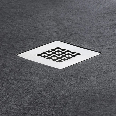 A square metal shower drain with a grid pattern, set into a dark gray slate-textured surface.