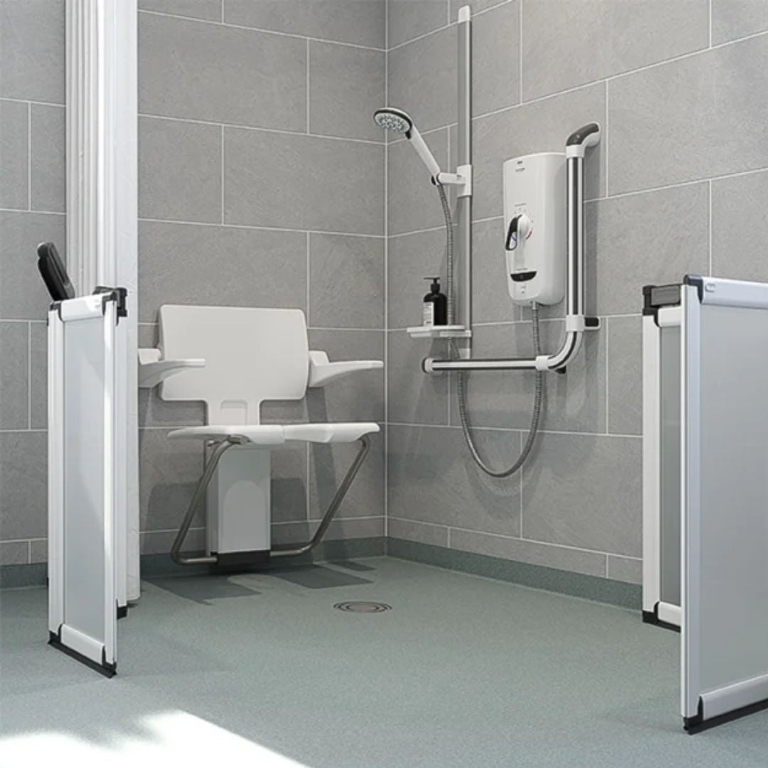 A modern wetroom shower setup with a white fold-down shower chair, wall-mounted shower system, gray tiled walls, vinyl floor and white-framed glass shower doors on both sides.