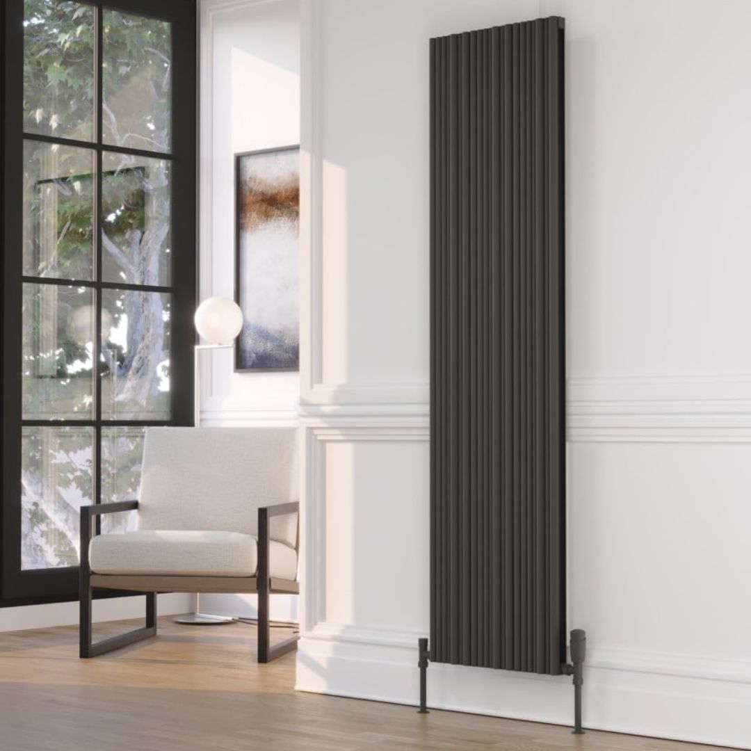 A tall, narrow dark grey radiator with a ribbed vertical design, mounted on a white wall in a modern living room setting.