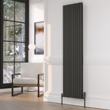 A tall, narrow dark grey radiator with a ribbed vertical design, mounted on a white wall in a modern living room setting.