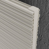 Close-up of a white radiator with a ribbed, wavy profile edge, shown against a dark gray textured wall background.