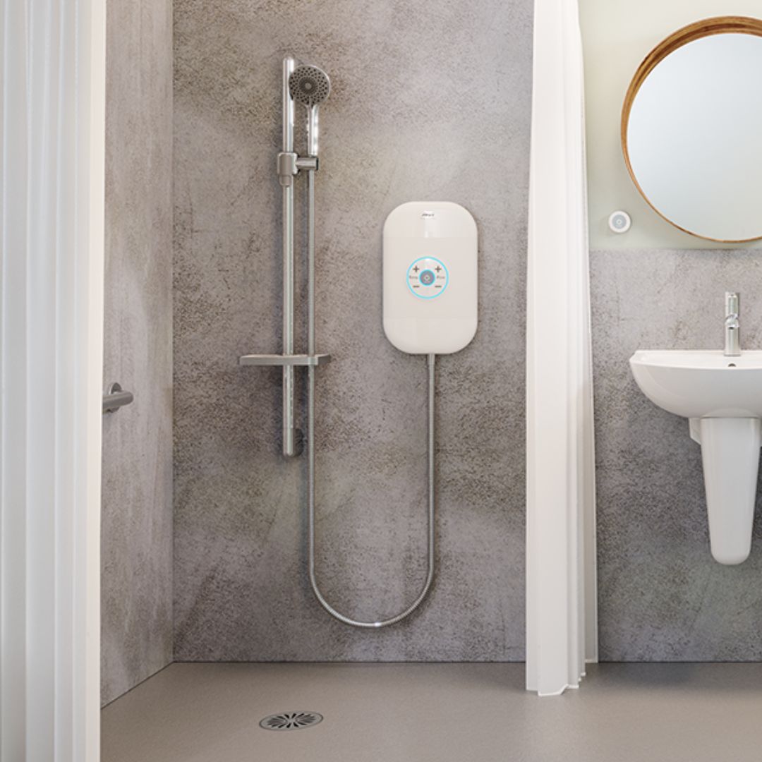 A modern wall-mounted electric shower system with a chrome shower head and hose, a white control box, and a gray textured shower wall in a bathroom setting.